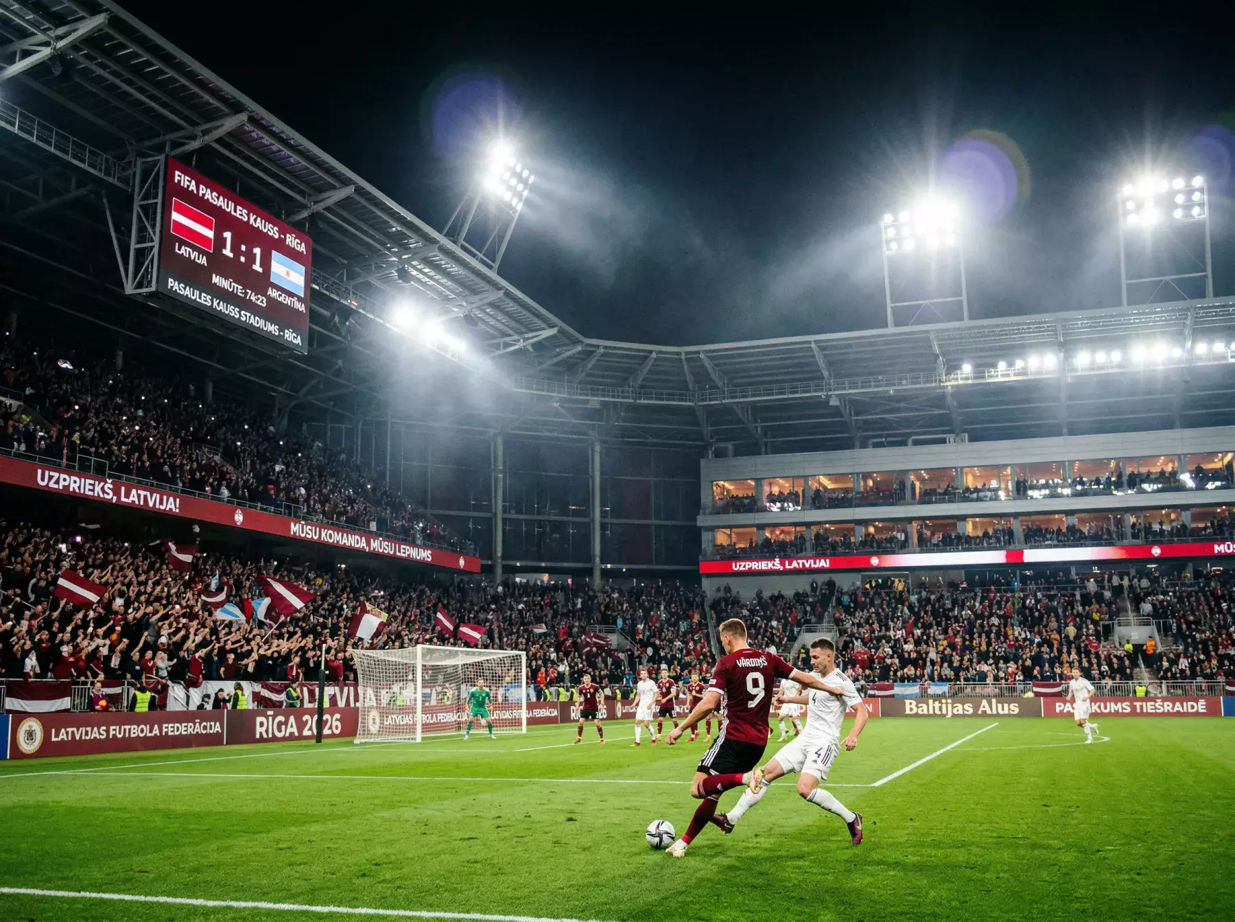 Futbola stadions ar faniem un spēli uz laukuma nakts apgaismojumā